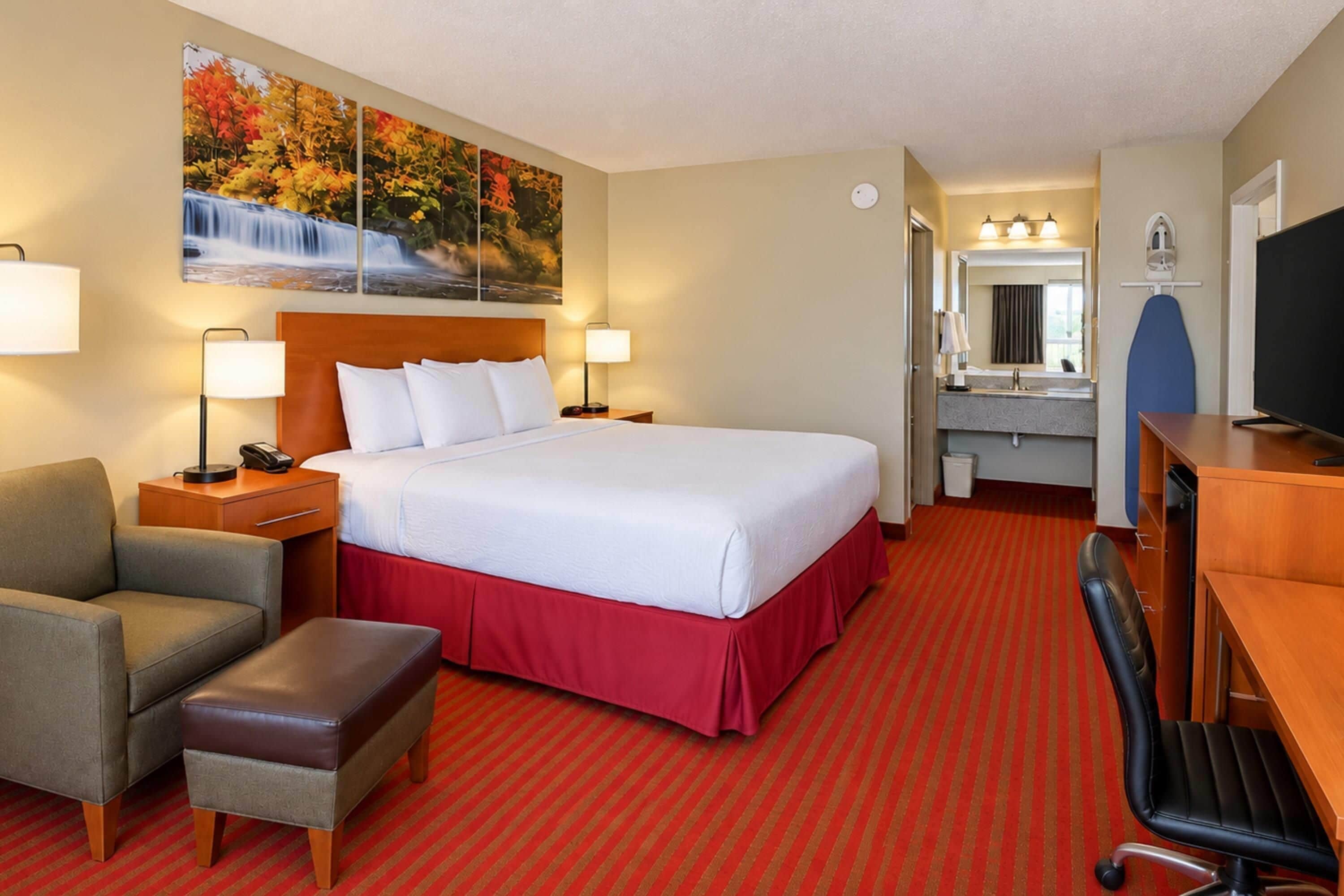 Une chambre d’hôtel avec un grand lit, un bureau, une chaise, un petit canapé, une télévision et une salle de bain équipée d’un miroir et d’un lavabo.