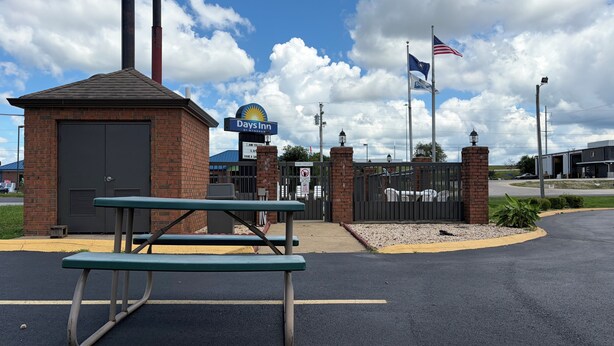 A Days Inn entrance with a picnic table, a gated parking area, and flags. - Days Inn by Wyndham Franklin (Franklin)