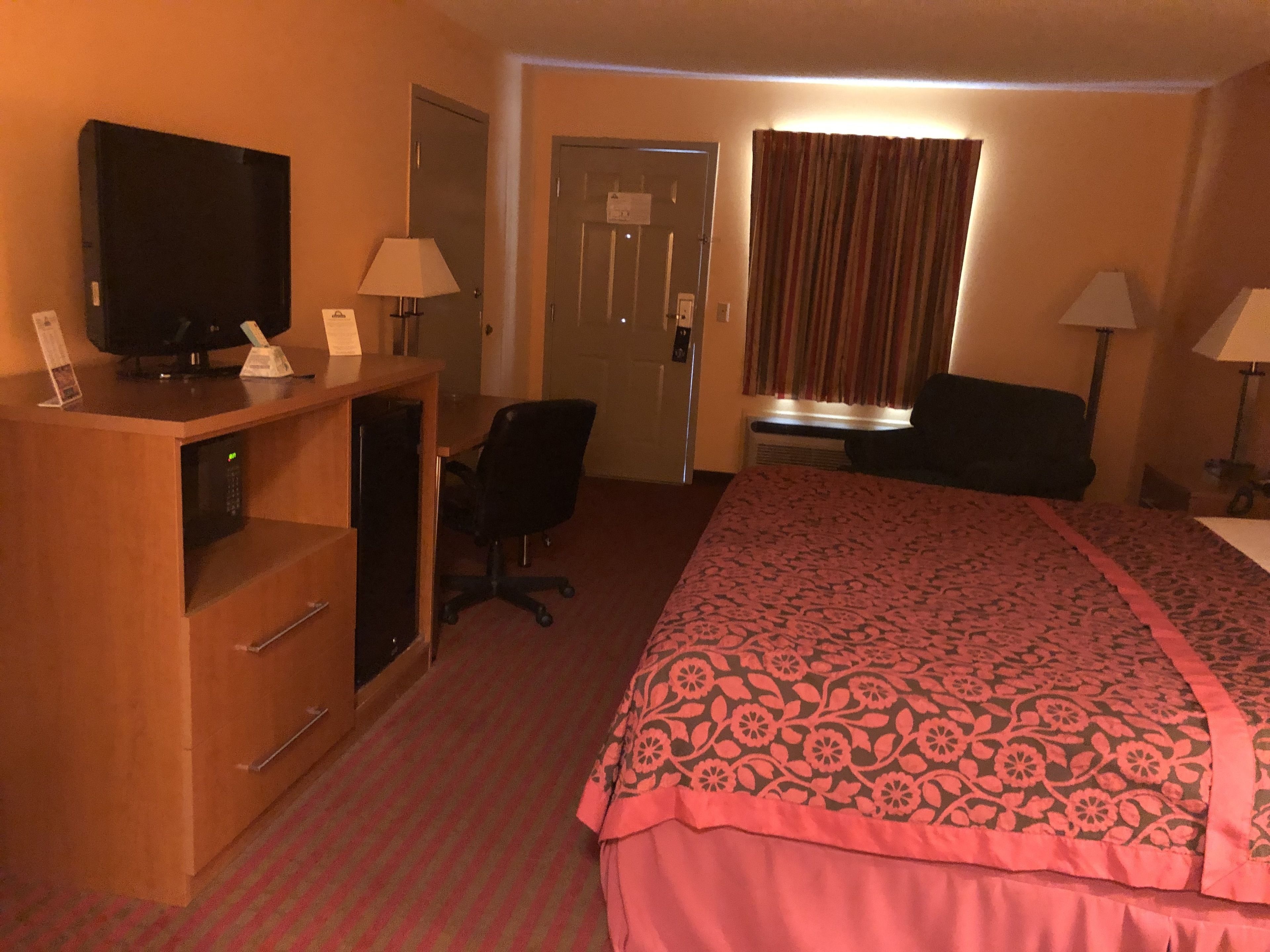A hotel room with a bed, desk, chair, television, and lamps.