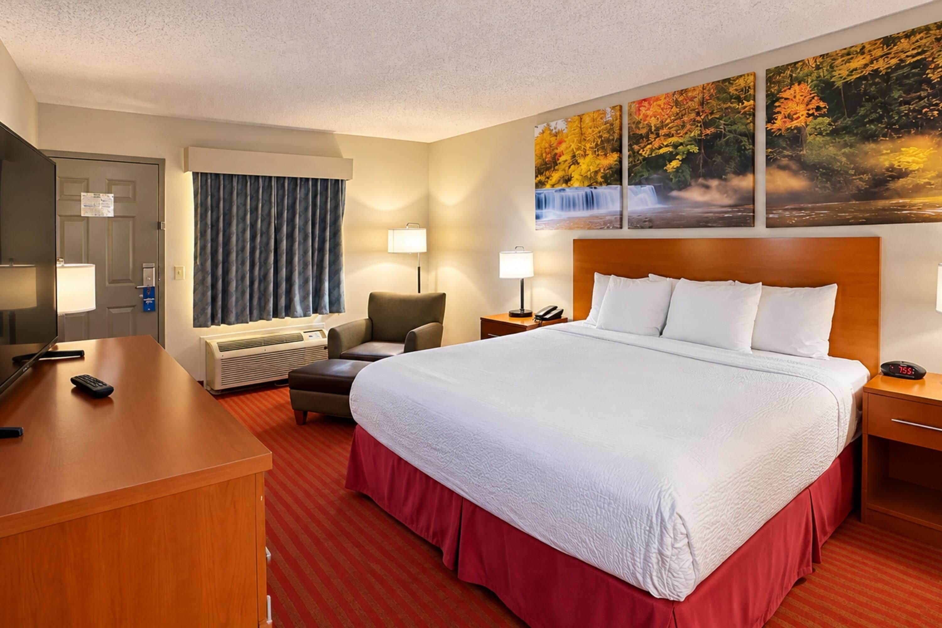 A hotel room with a bed, a desk, a chair, a TV, and a painting on the wall.