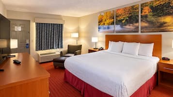 A hotel room with a bed, a desk, a chair, a TV, and a painting on the wall.