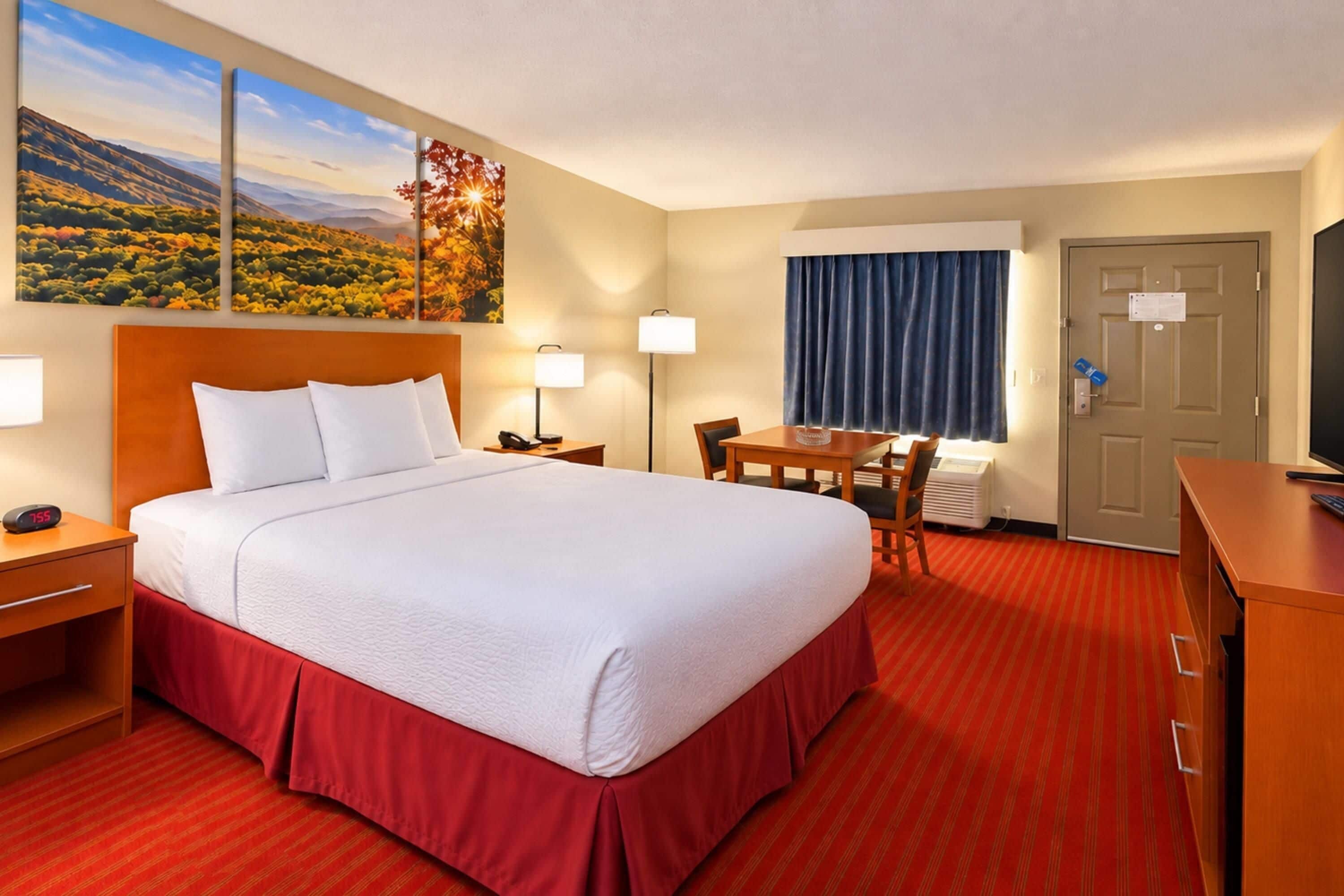 Een hotelkamer met een groot bed, een bureau, een stoel, een bureaulamp, een nachtkastje en een klok.