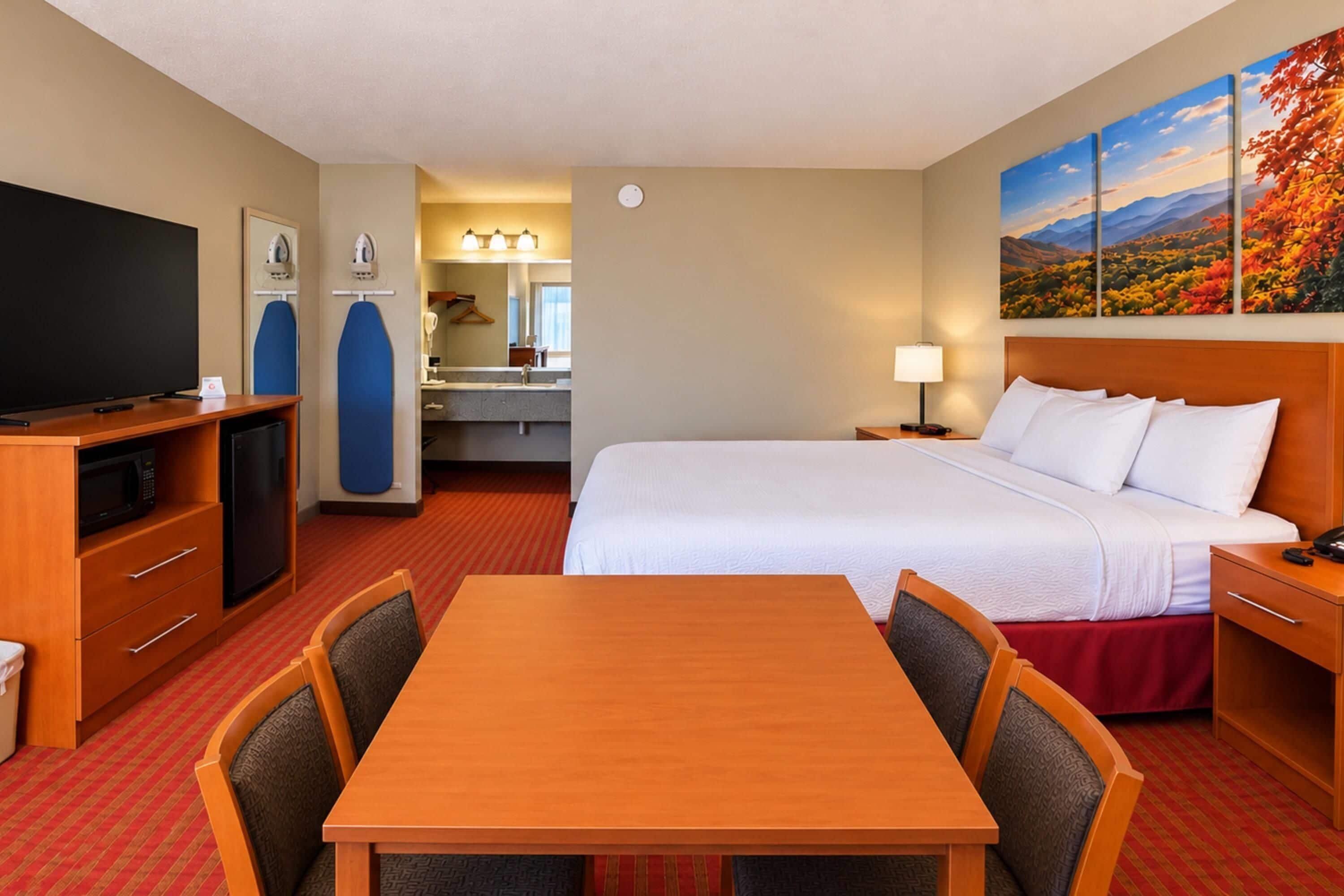 Une chambre d’hôtel équipée d’un lit, d’un bureau, d’une télévision, d’un four à micro-ondes et d’un coin repas avec des chaises.