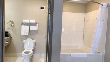 A bathroom with a toilet, a towel rack with towels, and a shower area with a bathtub.
