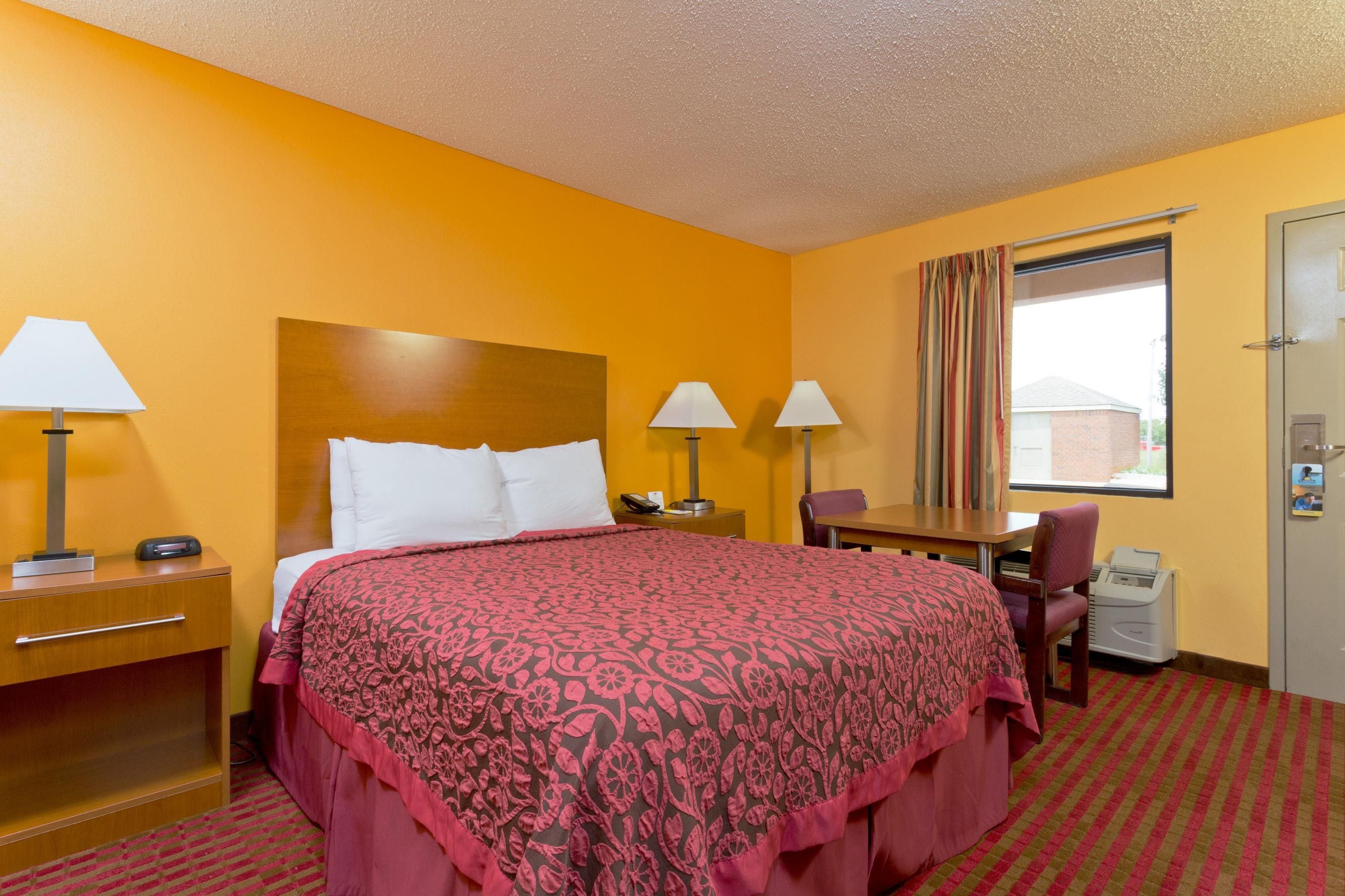 A hotel room with a bed, bedside lamps, a desk, a chair, and a window with curtains.