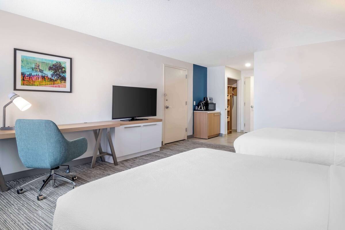 A hotel room with a desk, chair, TV, and two beds.