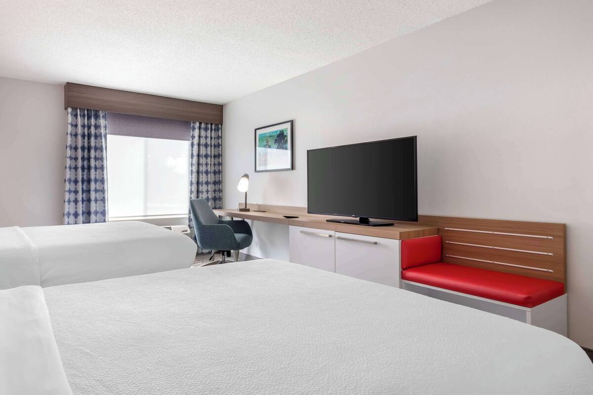 A hotel room with two beds, a desk, a television, and a window with curtains.