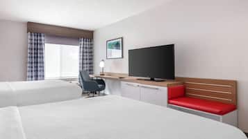 A hotel room with two beds, a desk, a television, and a window with curtains.