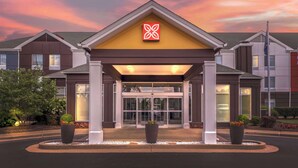A hotel entrance with a modern design, featuring a prominent logo above the entrance, a covered walkway, and potted plants at the entrance. - Hilton Garden Inn Lexington Hamburg (Lexington)