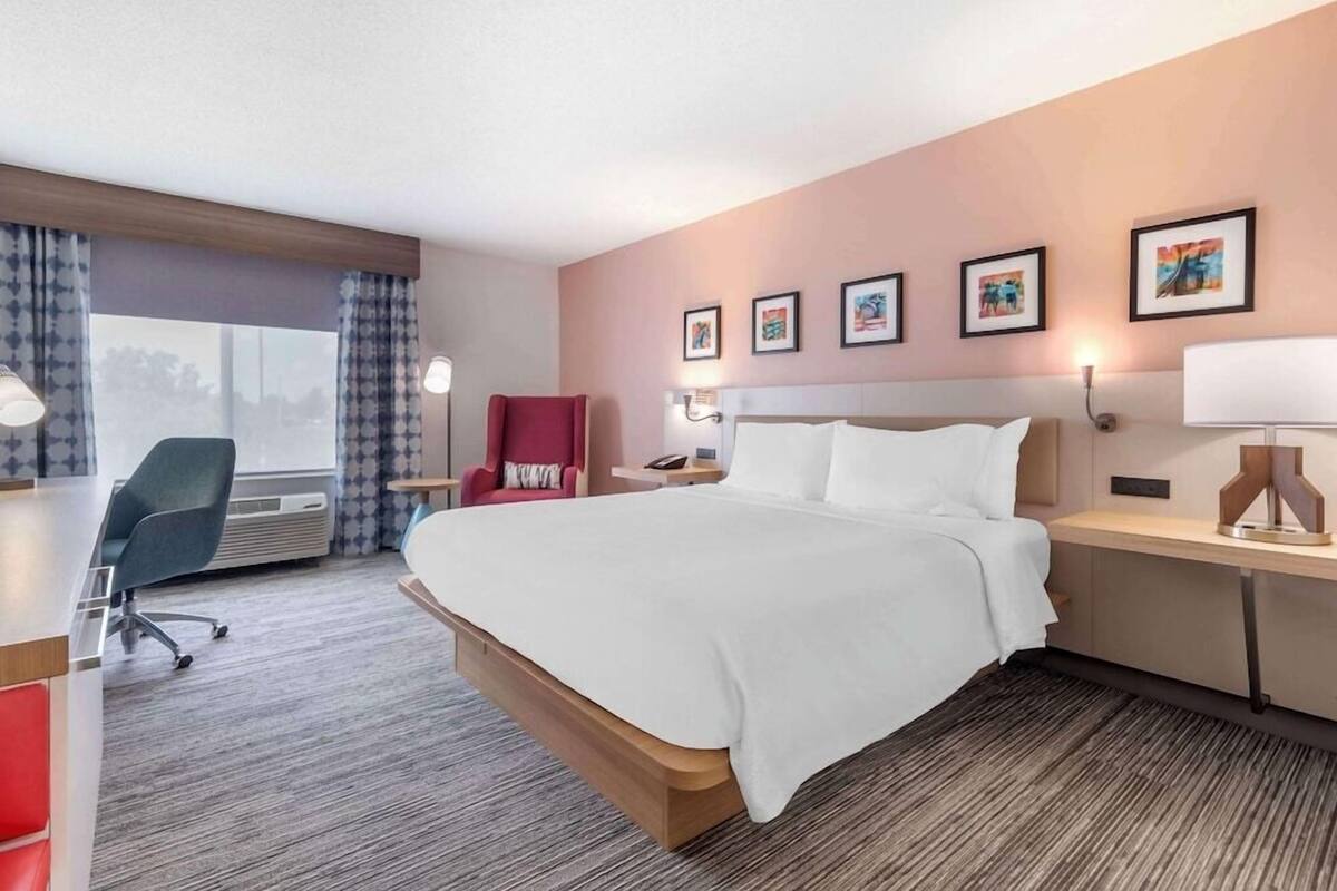 A hotel room with a large bed, a desk, a chair, and a window with curtains.