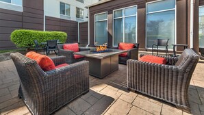 An outdoor patio area with wicker furniture, a central fire feature, and large windows. - Hilton Garden Inn Lexington Hamburg (Lexington)