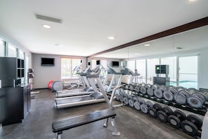 Un gimnasio con cintas de correr, una banca y un estante con mancuernas.
