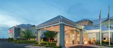 A hotel entrance with a covered waiting area, a clear sky, and a flagpole.