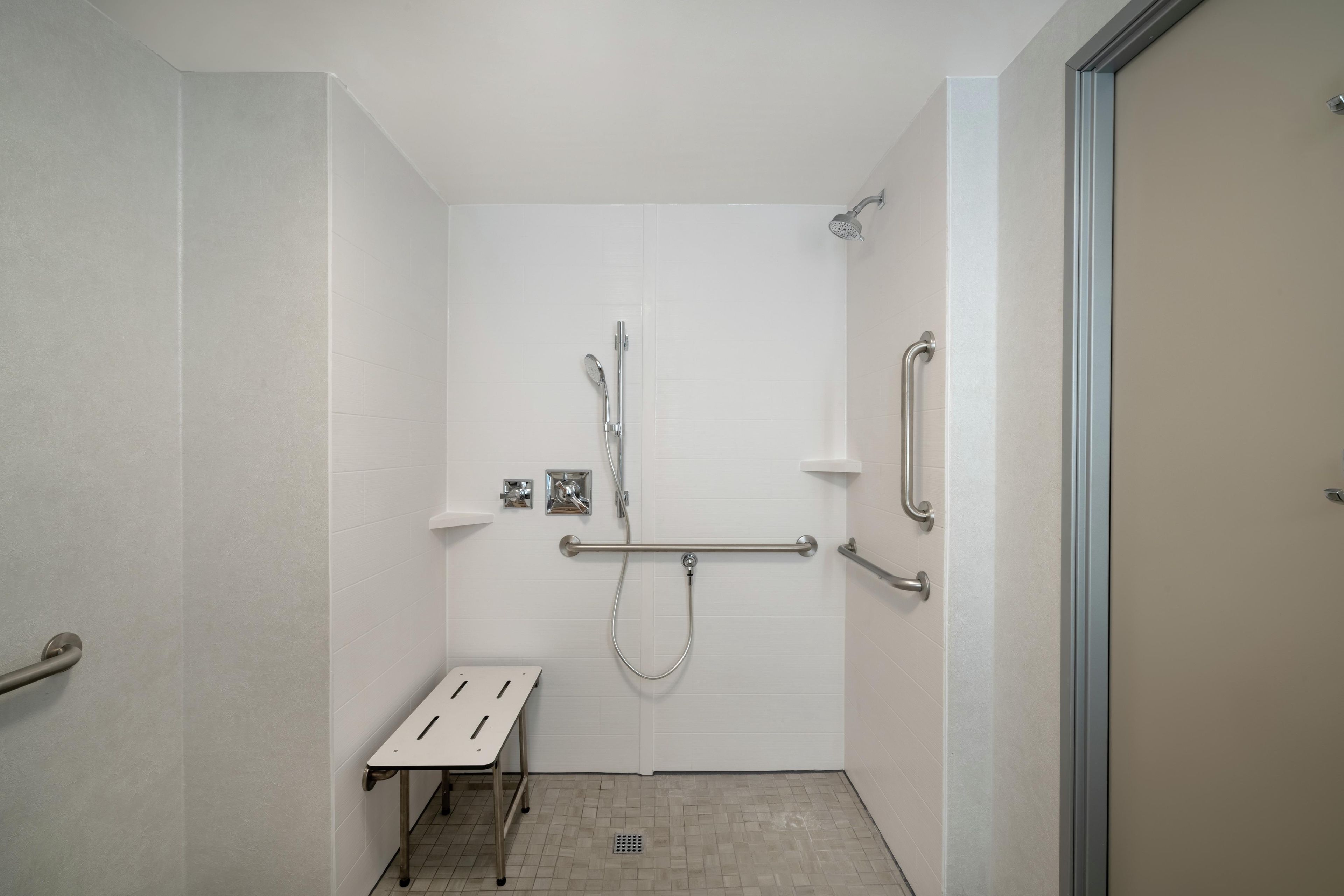 A small, enclosed shower area with a bench, grab bars, and a handheld showerhead.