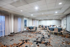 Un salón de conferencias con mesas dispuestas para una reunión, amplias ventanas con cortinas y una alfombra estampada.