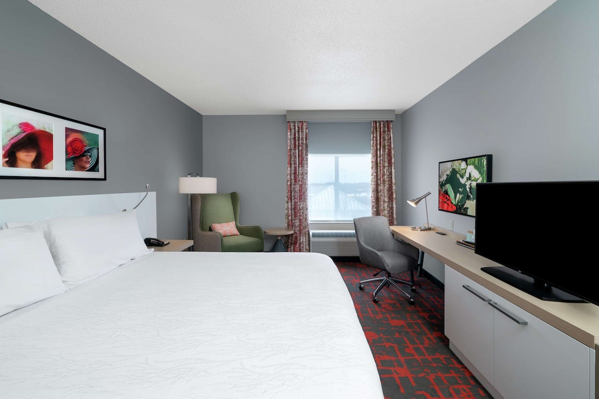 A hotel room with a large bed, a desk with a computer, a chair, and a TV.