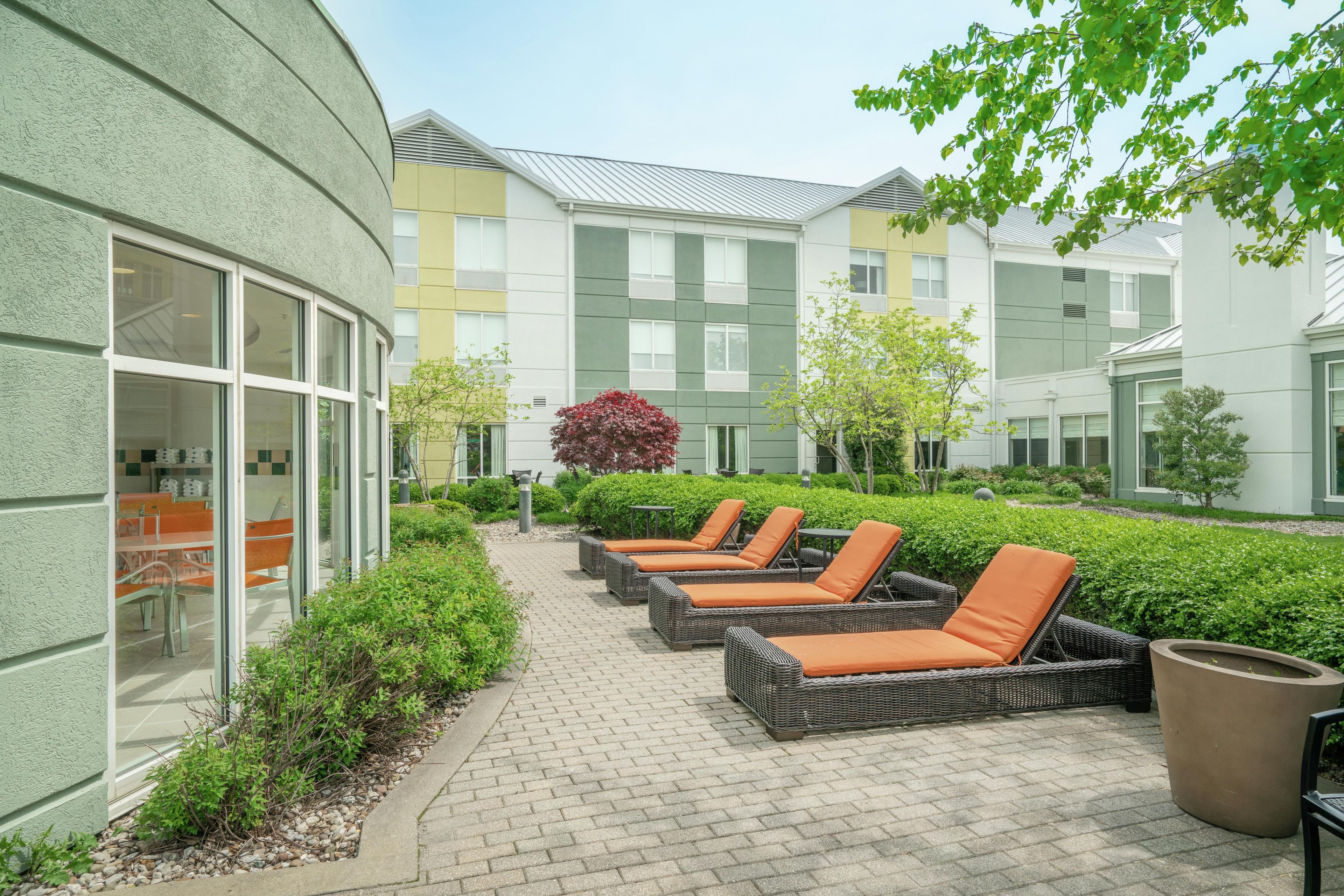 A courtyard with outdoor seating, a pathway, and buildings with large windows.