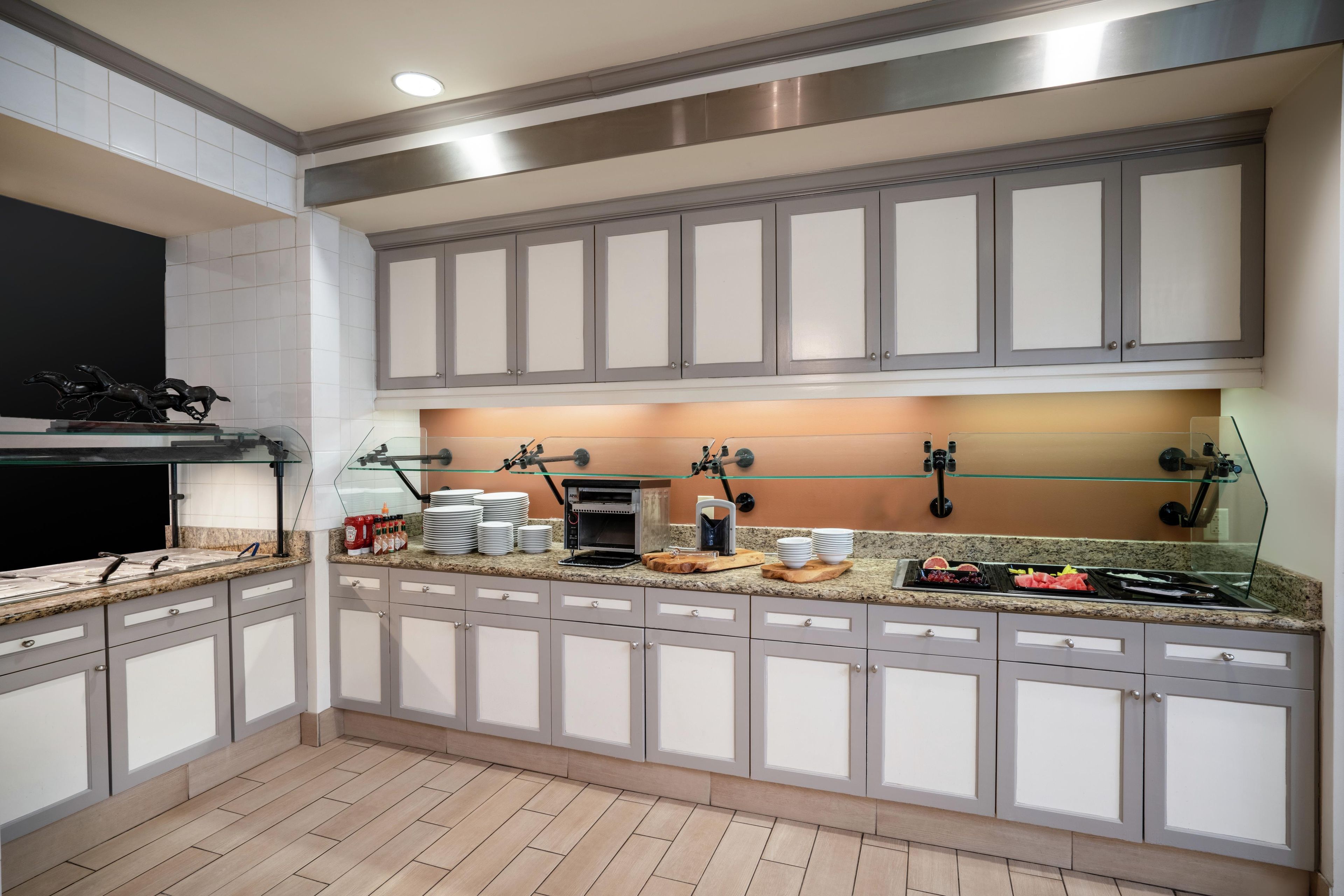 A modern kitchen with grey cabinets, a built-in oven, and a glass-top island with various kitchen items.