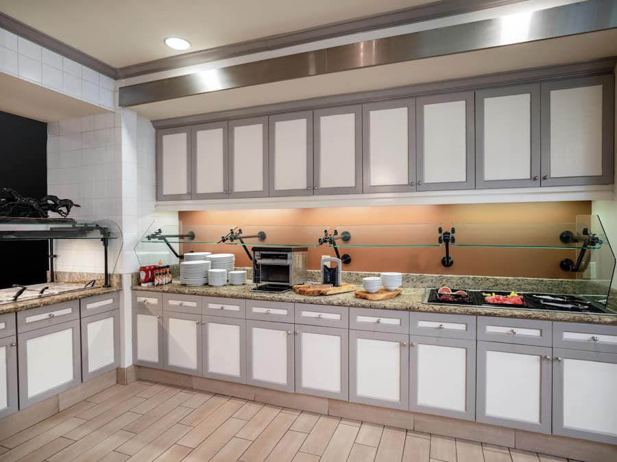 A modern kitchen with grey cabinets, a built-in oven, and a glass-top island with various kitchen items.