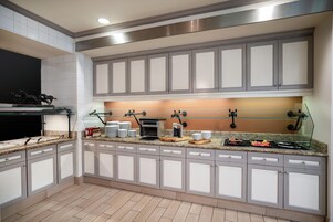 A modern kitchen with grey cabinets, a built-in oven, and a glass-top island with various kitchen items.