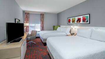 Habitación de hotel con dos camas, televisión, escritorio y ventana con cortinas.