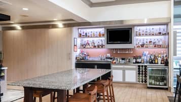 Zona de bar con encimera de granito, taburetes de madera y una variedad de botellas de licor.