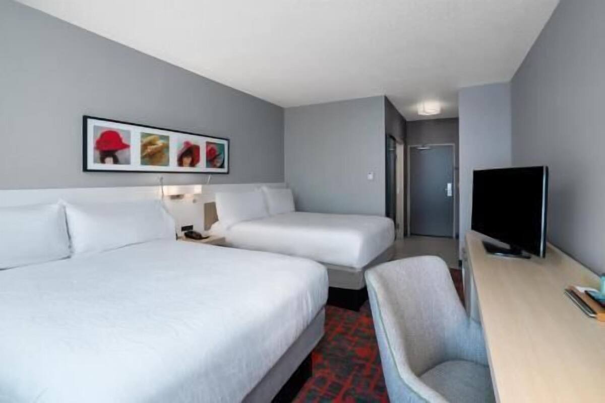 Habitación de hotel con dos camas, un escritorio con televisor y una silla.