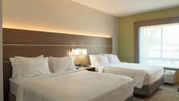 A hotel room with two beds, a nightstand, a lamp, and a window with a view.