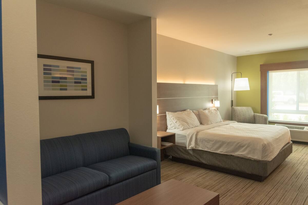 A hotel room with a bed, a blue sofa, a bedside table, a lamp, and a framed picture on the wall.