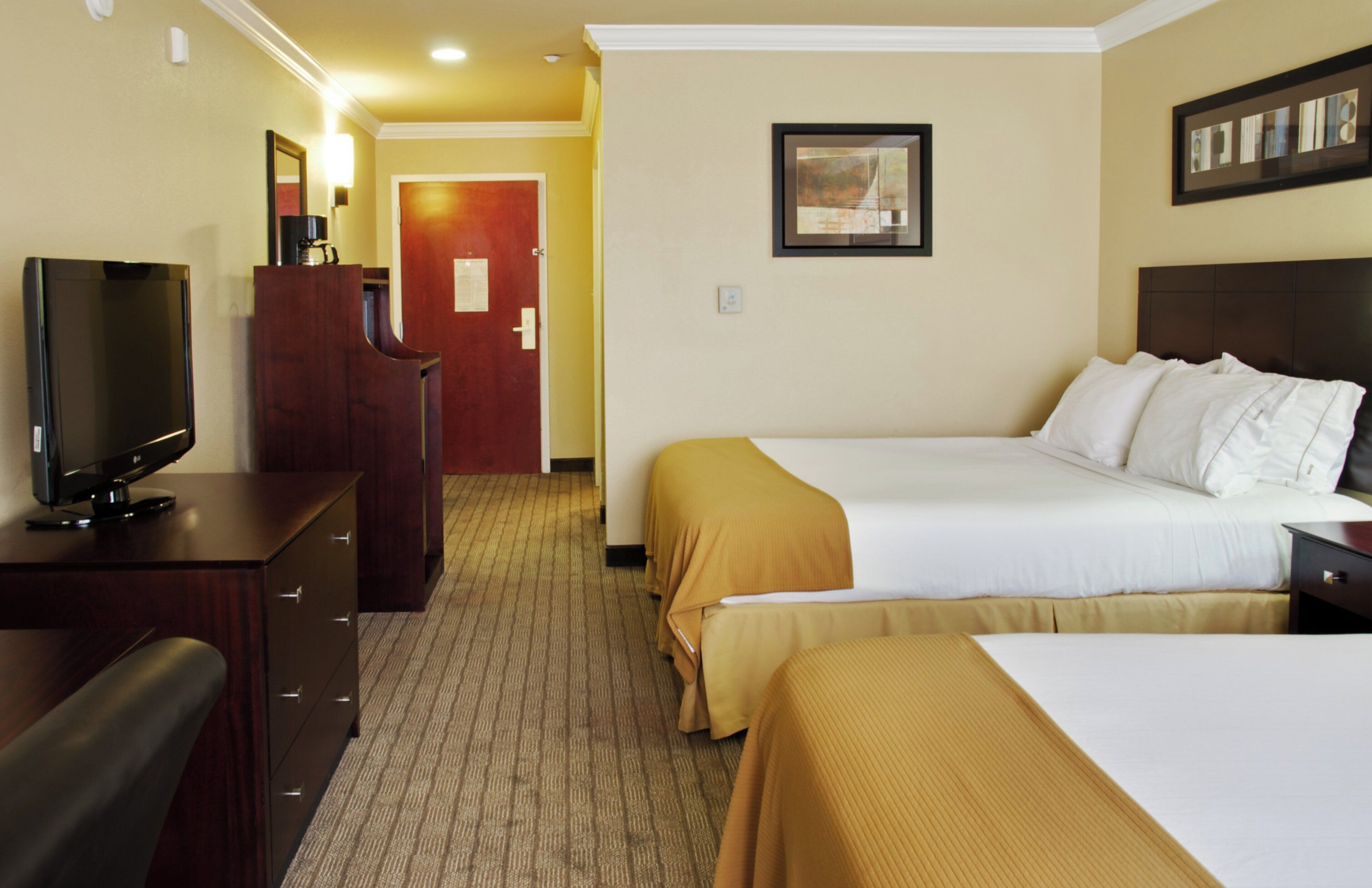 Habitación de hotel con cama, escritorio con televisor, armario y puerta que da a otra habitación.