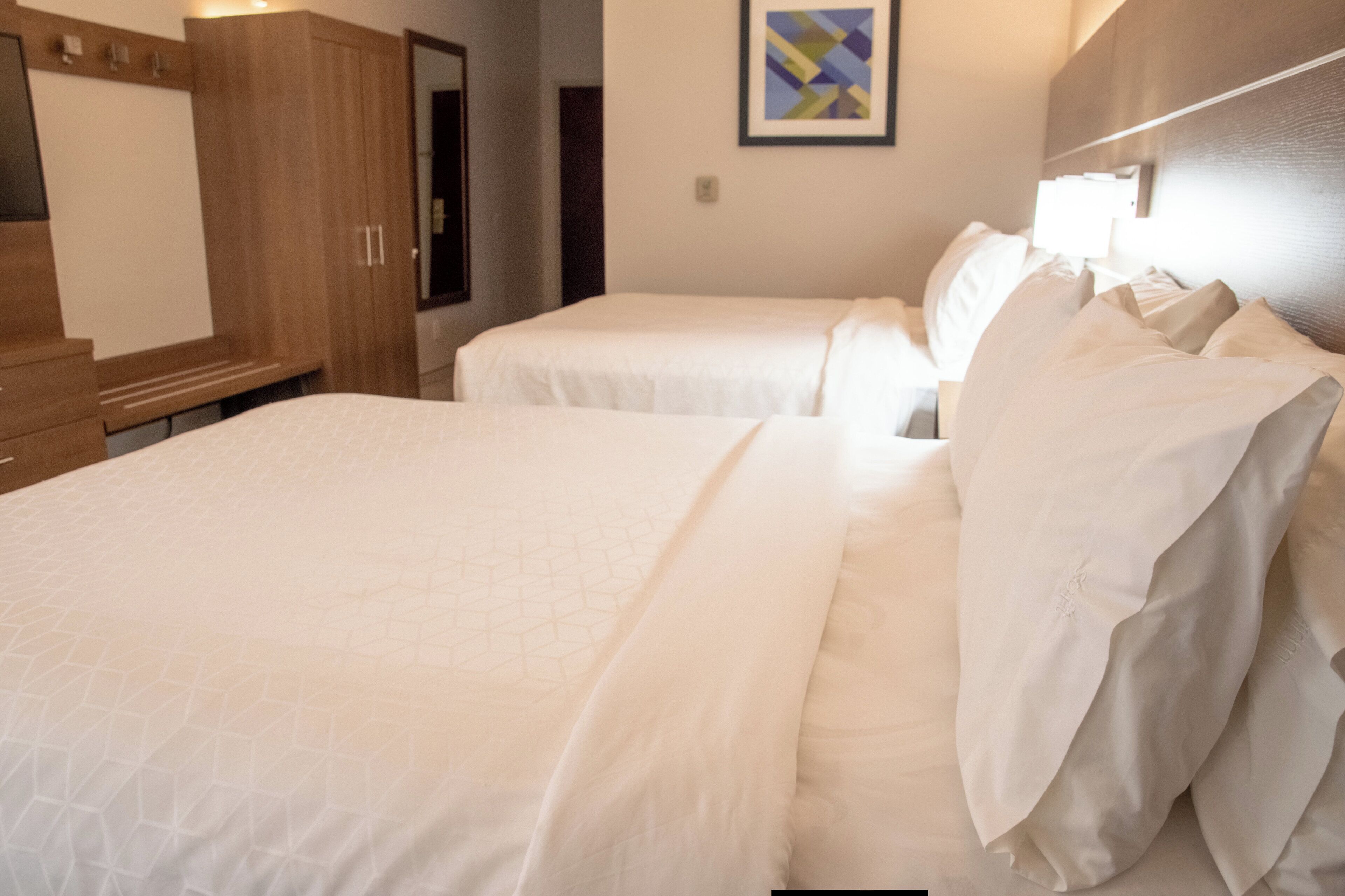 A hotel room with two beds, a wardrobe, a mirror, and a framed picture on the wall.