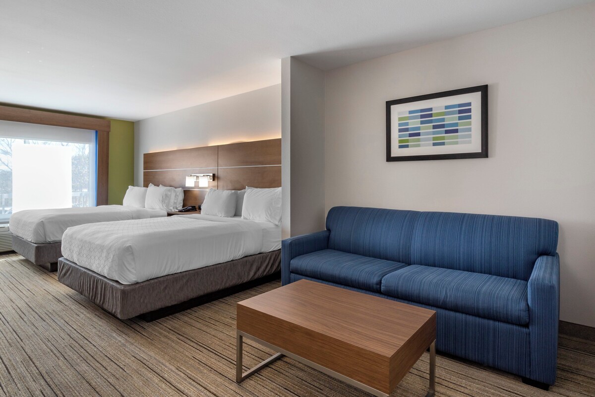 Une chambre d’hôtel avec deux lits, un canapé bleu, une table basse en bois et une œuvre d’art abstraite encadrée accrochée au mur.
