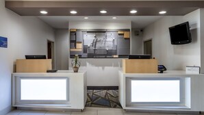 A hotel reception area with two reception desks, a digital display, a flat-screen TV, and a sign indicating the hotel name.