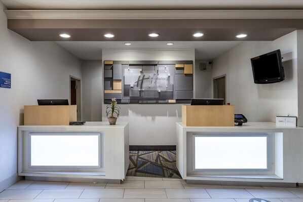 A hotel reception area with two reception desks, a digital display, a flat-screen TV, and a sign indicating the hotel name. - Holiday Inn Express Hotel & Suites Natchitoches by IHG (Natchitoches)