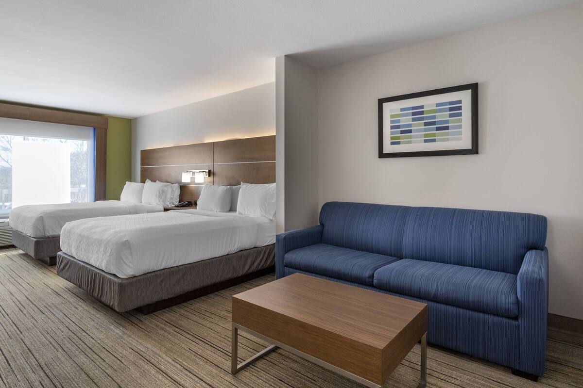 A hotel room with two beds, a blue sofa, a wooden coffee table, and a framed abstract art piece on the wall.