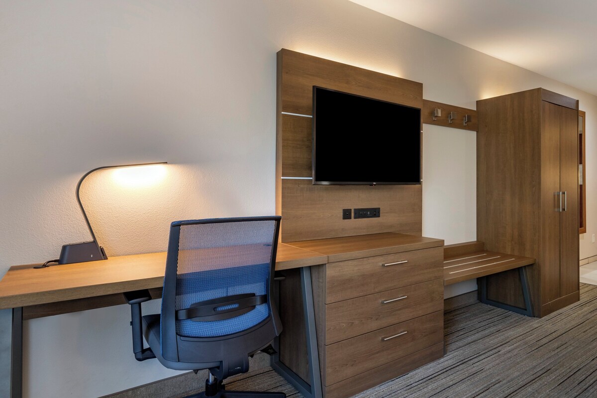 Une chambre d’hôtel moderne équipée d’un bureau en bois, d’une chaise, d’un téléviseur à écran plat fixé au mur et d’une armoire.