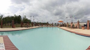 Une piscine entourée d’une clôture et de piliers en briques, avec des chaises longues et des parasols.