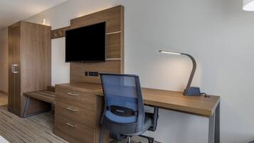 Una habitación de hotel moderna con un escritorio de madera, un televisor de pantalla plana, una silla de oficina de malla azul, una lámpara de escritorio y un armario.