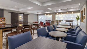 Un comedor moderno con varias mesas y sillas, una zona de cocina con mostrador, y ventanas amplias que ofrecen luz natural.