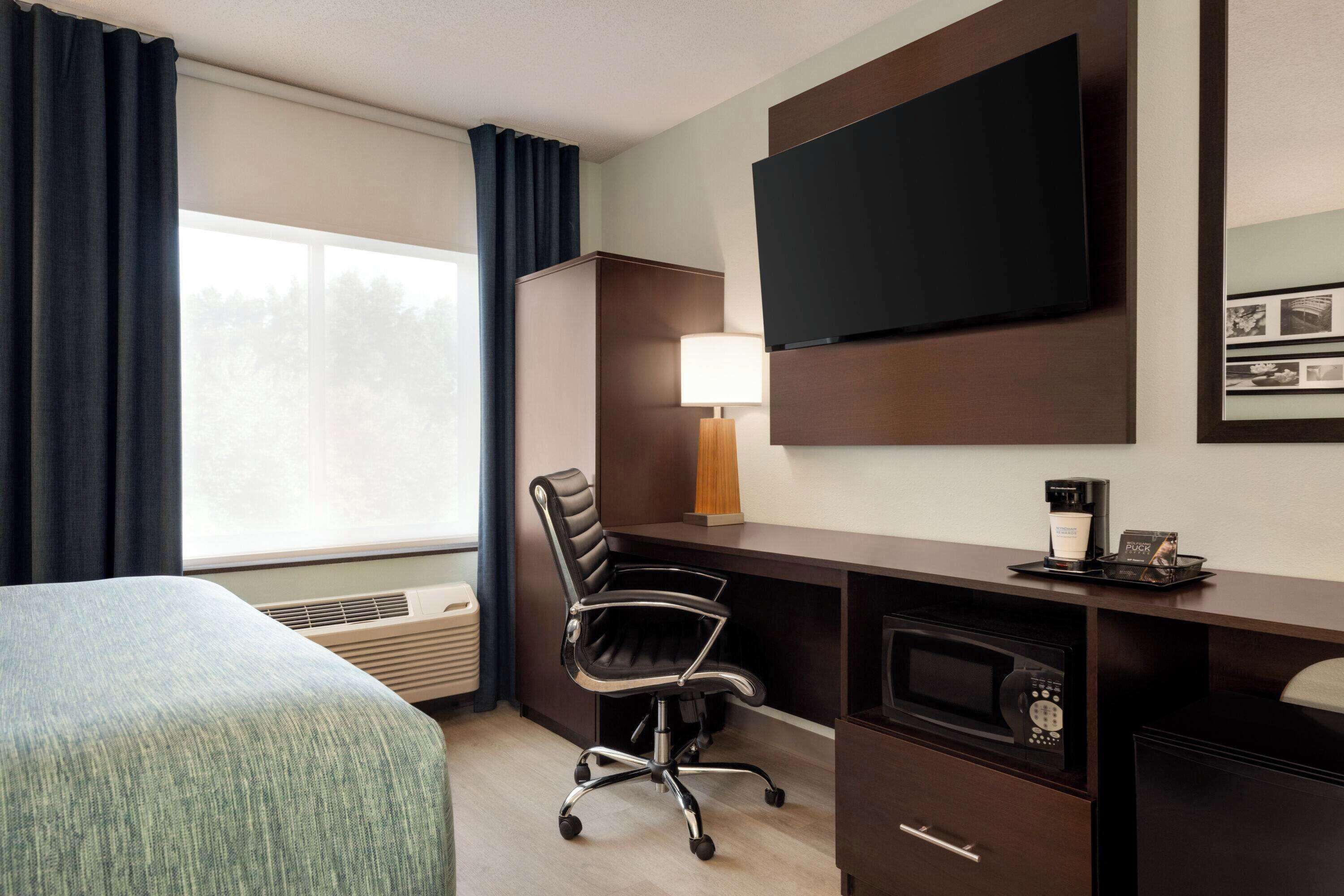 Habitación de hotel con cama, escritorio con computadora, televisión, lámpara y cafetera.