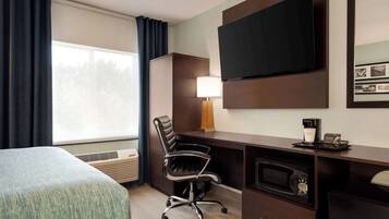 A hotel room with a bed, a desk with a computer, a TV, a lamp, and a coffee maker.