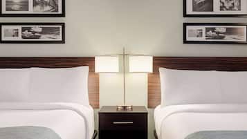 A hotel room with two beds, a nightstand with two lamps, and framed pictures on the wall.