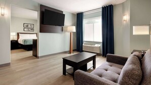 A hotel room with a bed, a TV mounted on the wall, a desk with a lamp, a sofa, and a window with curtains. - Wingate by Wyndham Salisbury MD Airport North (Salisbury)