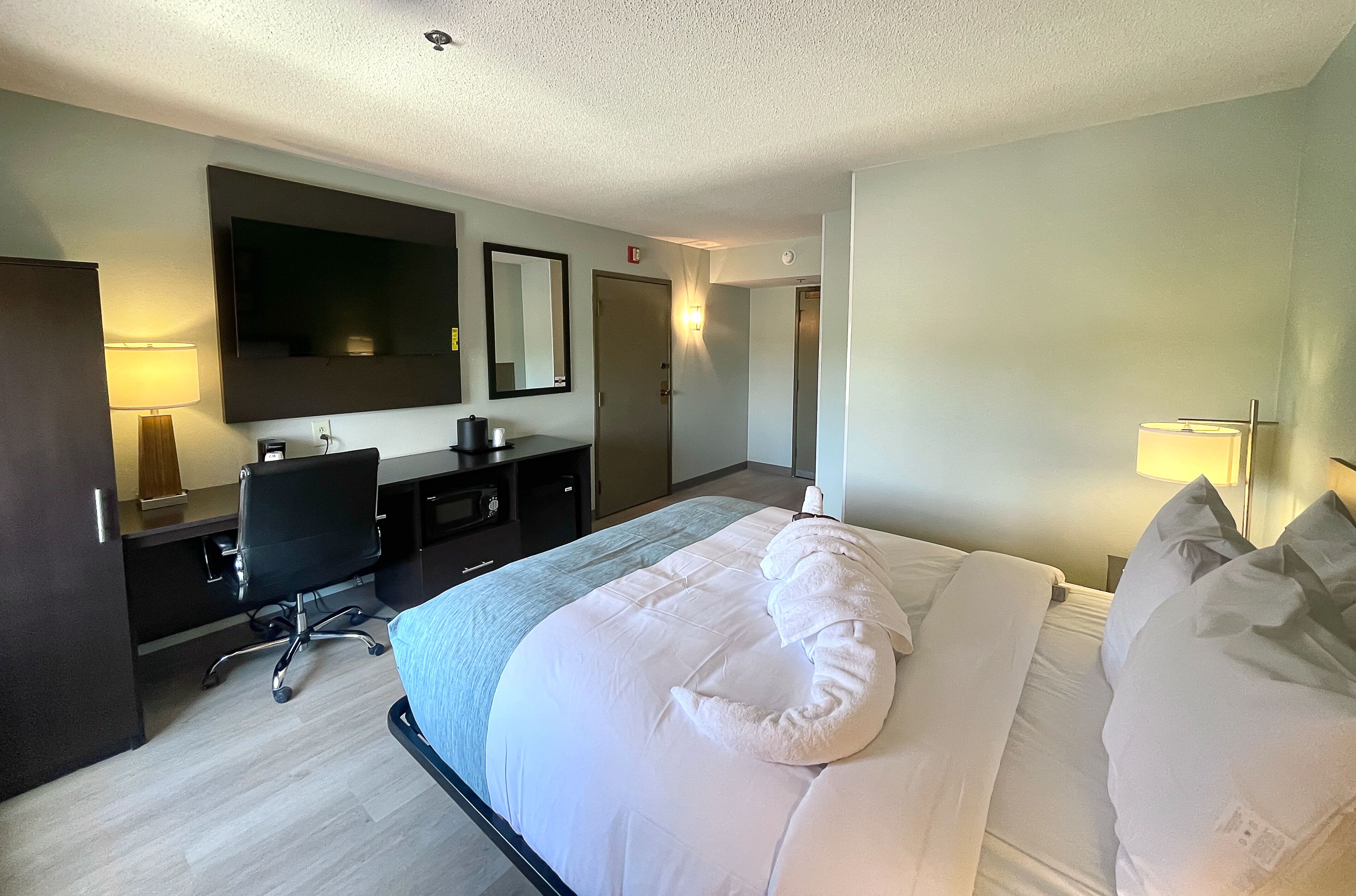 Une chambre d’hôtel avec un grand lit, un bureau avec une chaise, un téléviseur à écran plat fixé au mur et un miroir au-dessus du bureau.