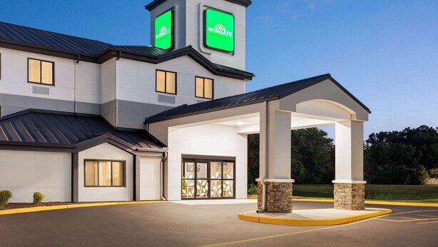A modern hotel with a prominent wingate logo, a covered entrance, and a parking lot.