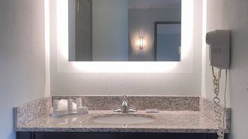 A bathroom with a granite countertop sink, a large mirror, and a hairdryer mounted on the wall.