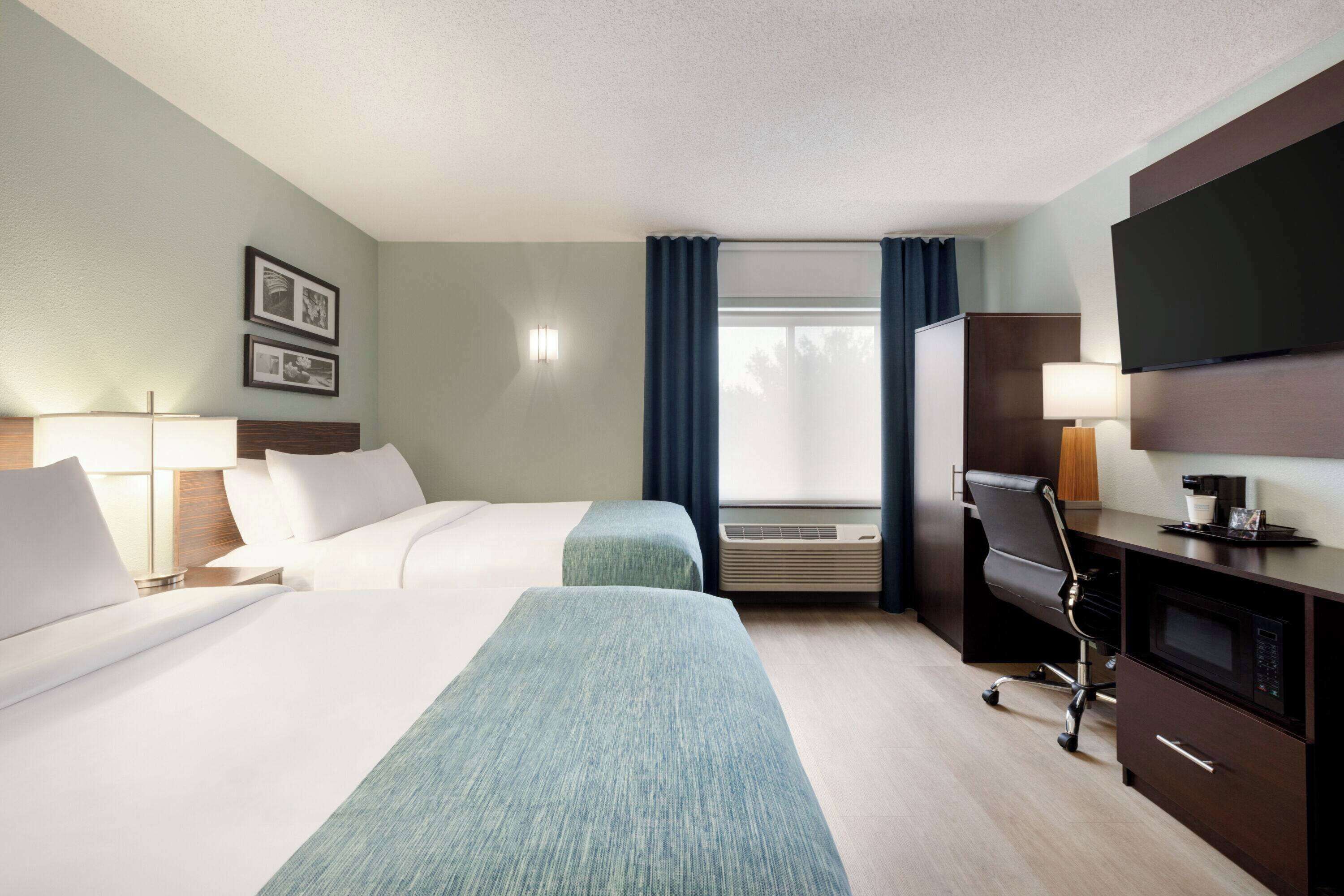 A hotel room with two beds, a desk, a television, and a window with curtains.