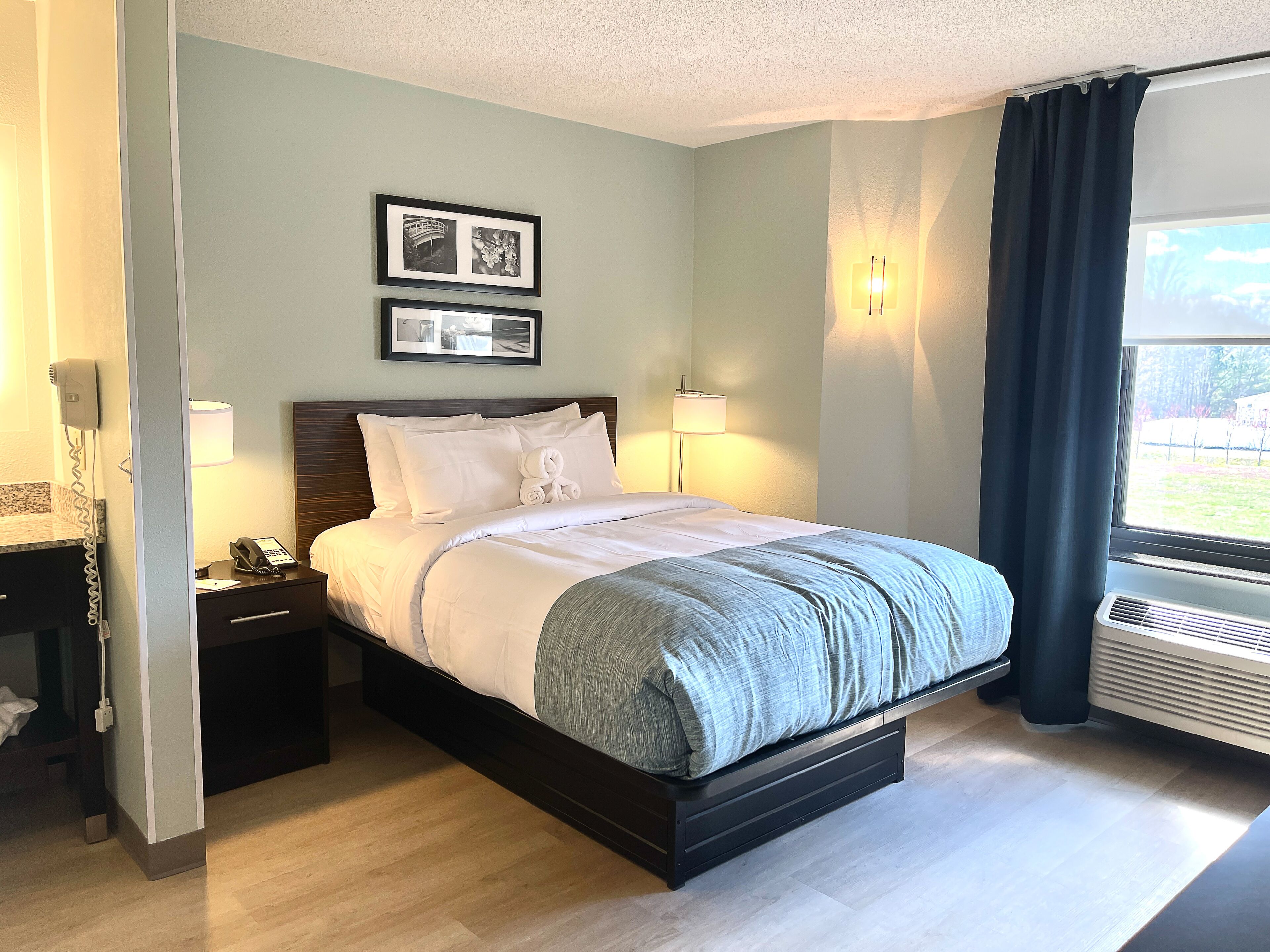 A hotel room with a bed, bedside lamps, a phone, a picture frame, and a window with curtains.