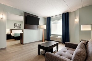 A hotel room with a flat-screen TV mounted on the wall, a bed with a headboard, a bedside table with a lamp, a seating area with a sofa and armchair, and a large window with curtains. - Wingate by Wyndham Salisbury MD Airport North (Salisbury)