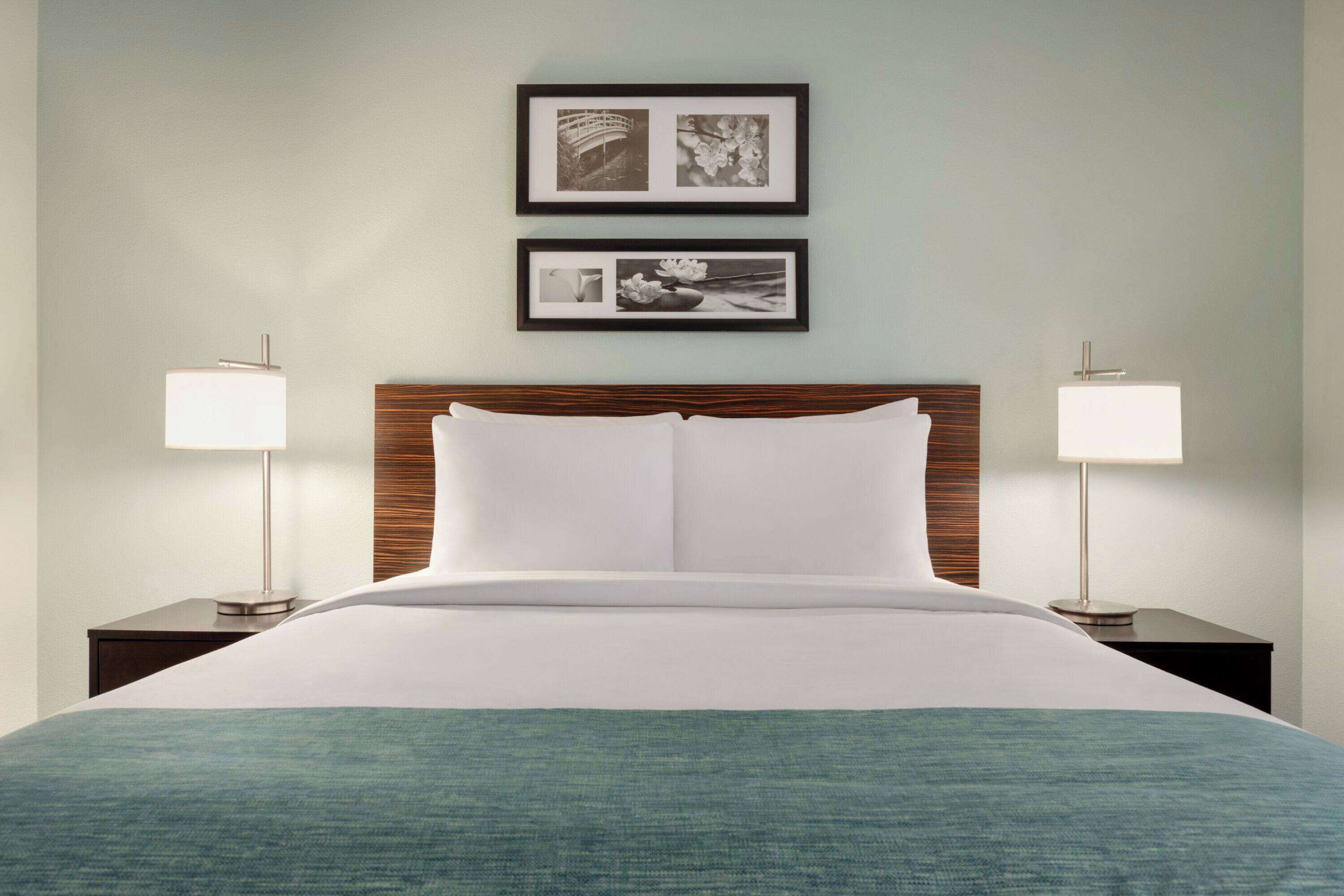 A neatly made bed with a wooden headboard, two bedside tables with lamps, and two framed pictures on the wall.